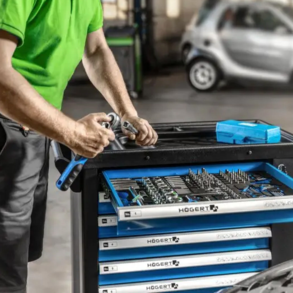 Mechanik pracujący przy wózku warsztatowym Högert trzymający grzechotkę z nasadką.
